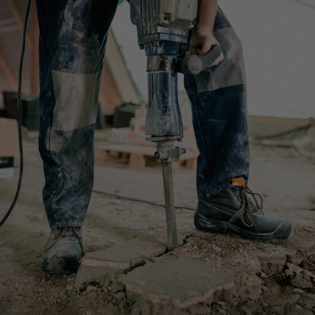 Construction worker using a jackhammer to break concrete, preparing for professional masonry deconstruction services in Seattle Washington.