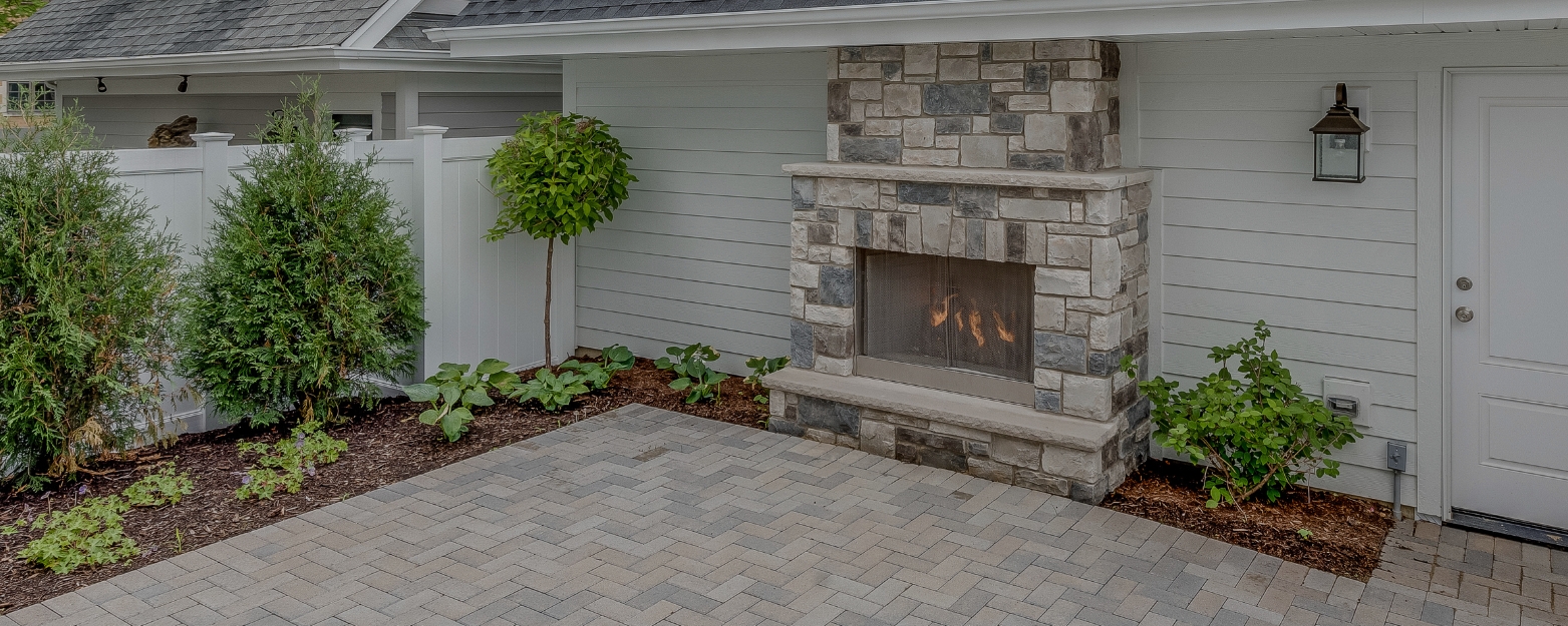 Outdoor stone fireplace with custom masonry and a herringbone paver patio in a beautifully landscaped backyard in Redmond, WA.